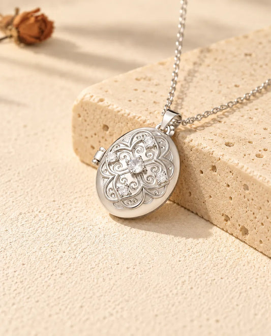 Personalized oval photo locket necklace in silver with a filigree flower lid and cubic zirconia, resting on a travertine block
