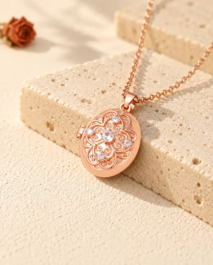 Rose gold tone oval photo locket with a cubic zirconia flower lid resting on travertine