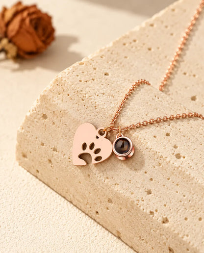 Rose gold tone paw print heart and projection stone charm resting against a travertine block