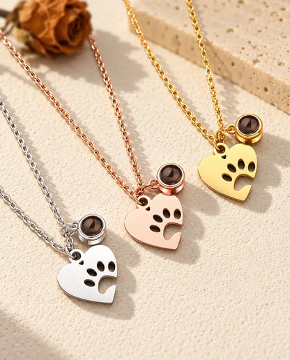 Three colors of the paw print heart pet projection necklace on a diagonal on cream plaster