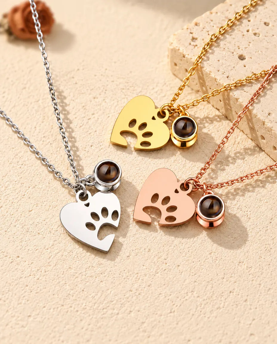 Silver tone, gold tone and rose gold tone paw heart necklaces arranged by a travertine slab