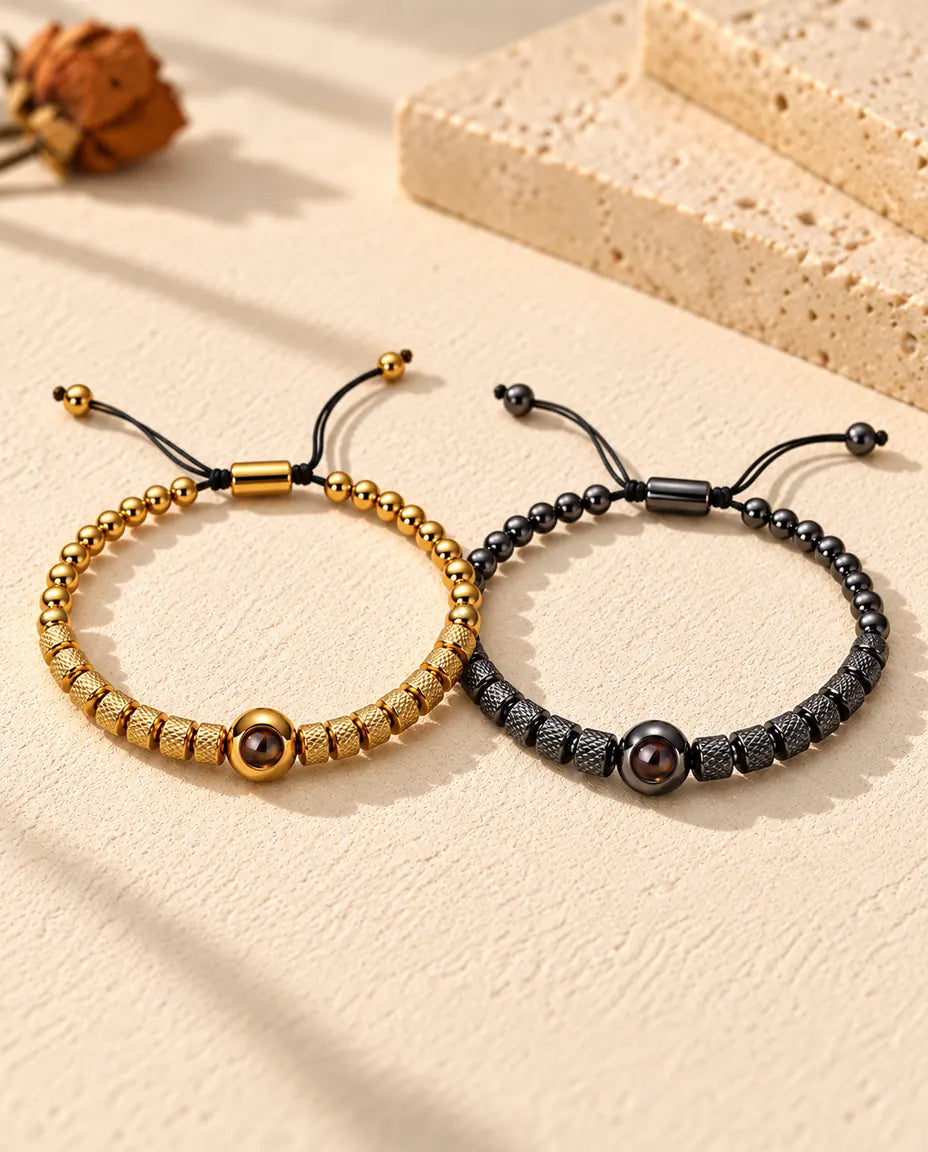 Personalized couples photo projection bracelets, a matching set of two textured bead bracelets in gold tone and black on cream plaster