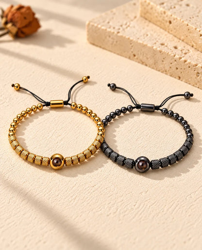 Personalized couples photo projection bracelets, a matching set of two textured bead bracelets in gold tone and black on cream plaster