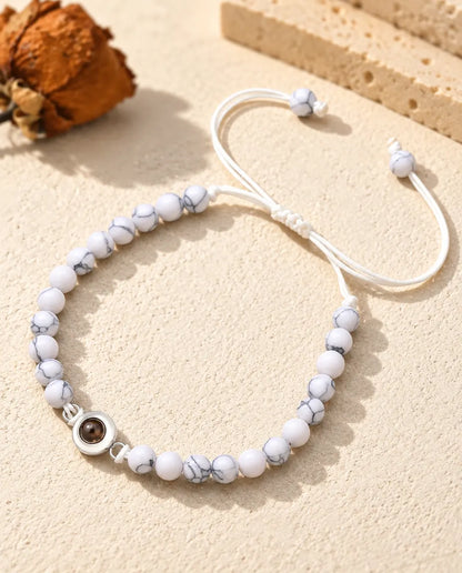 White marbled bead bracelet with a silver tone projection charm and sliding knot