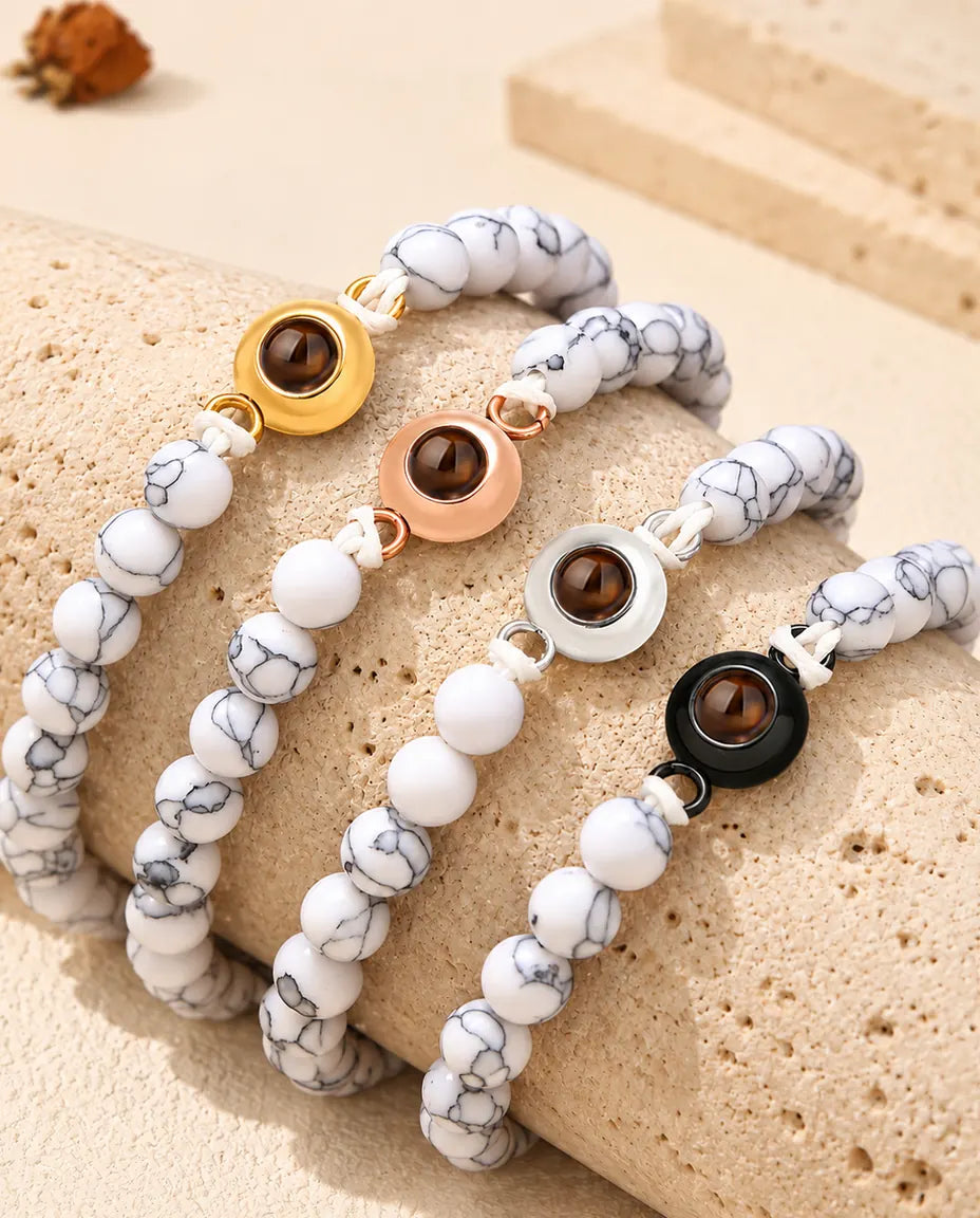 White marbled bead projection bracelets in each charm color draped over travertine