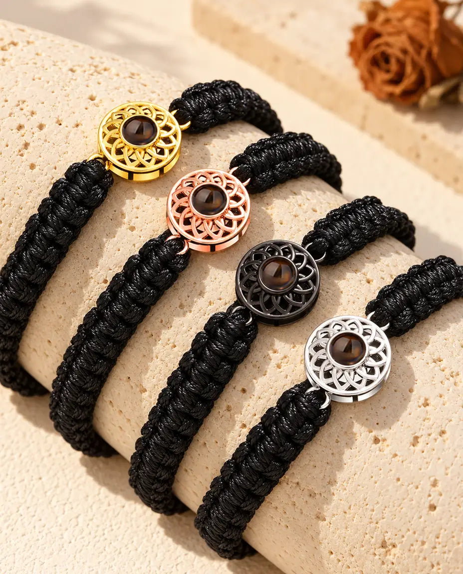 Four black braided cord bracelets showing every charm color draped over travertine