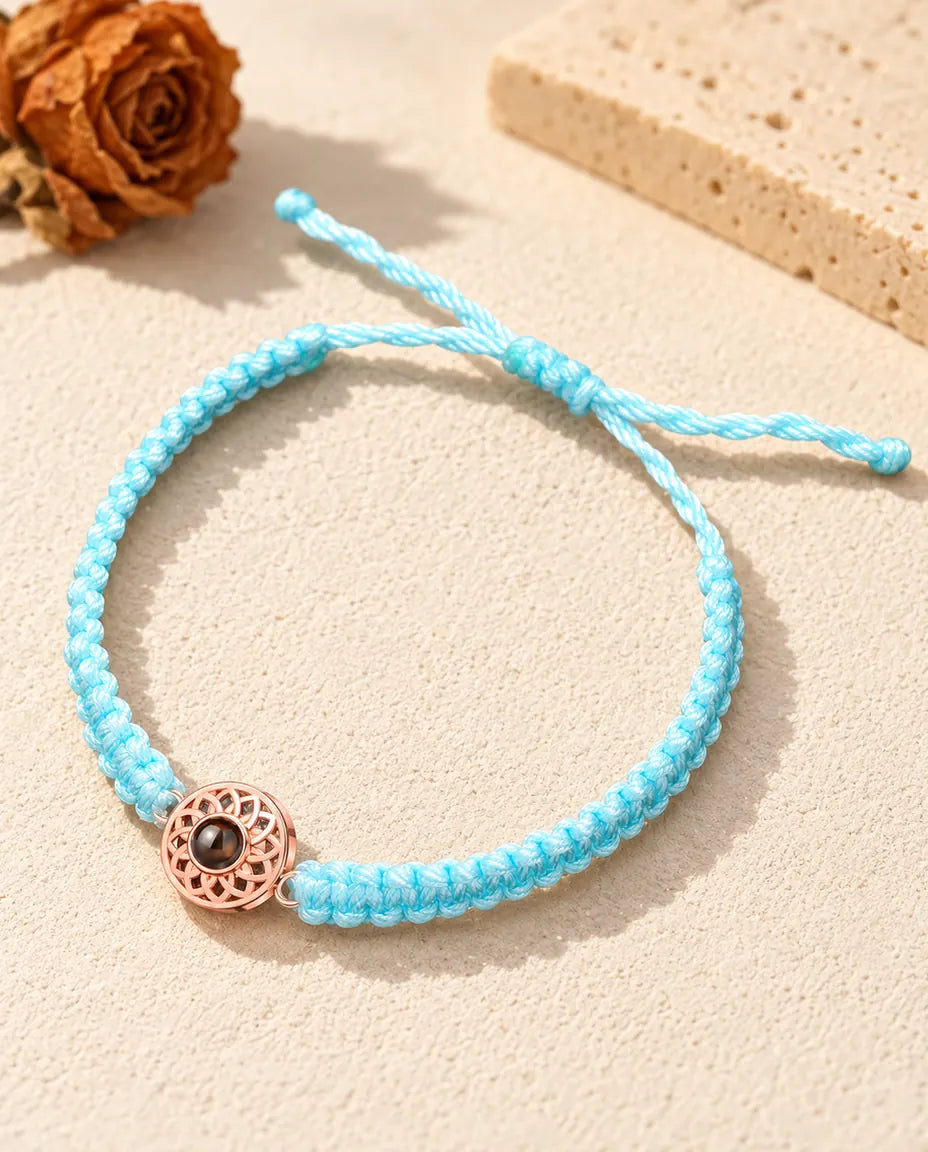 Rose gold tone round charm on a light blue braided cord with adjustable sliding knot