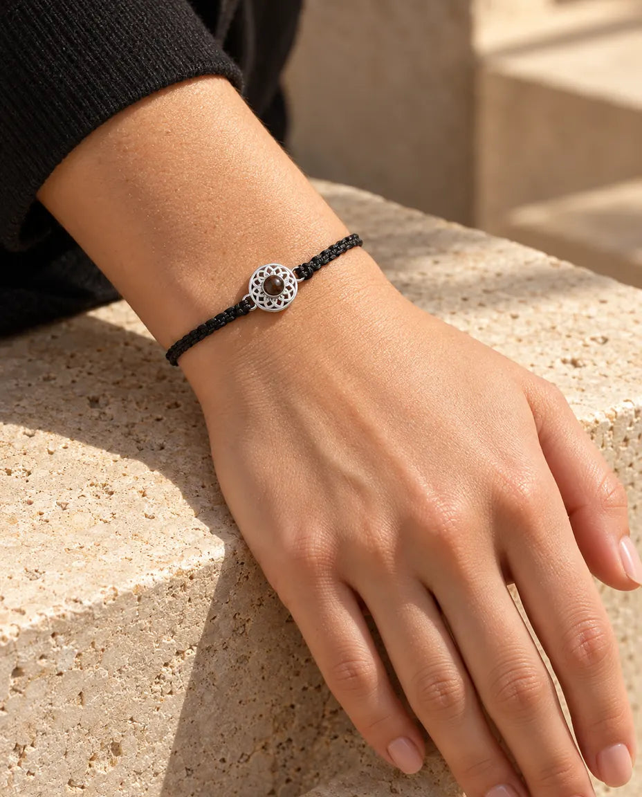 Woman wearing the black thin braided cord bracelet with a silver tone round charm on her wrist in warm sunlight