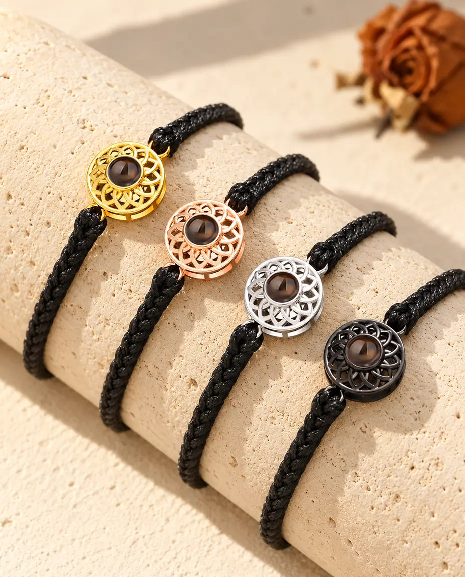 Four black thin braided cord bracelets showing every charm color draped over travertine