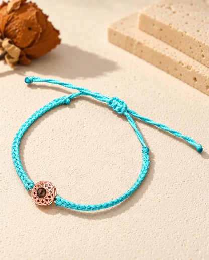 Rose gold tone round charm on a blue thin braided cord with adjustable sliding knot