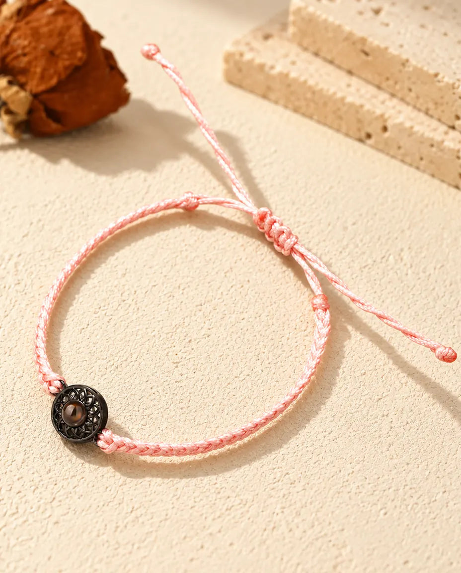 Pink thin braided cord bracelet with a black round charm holding a brown projection stone