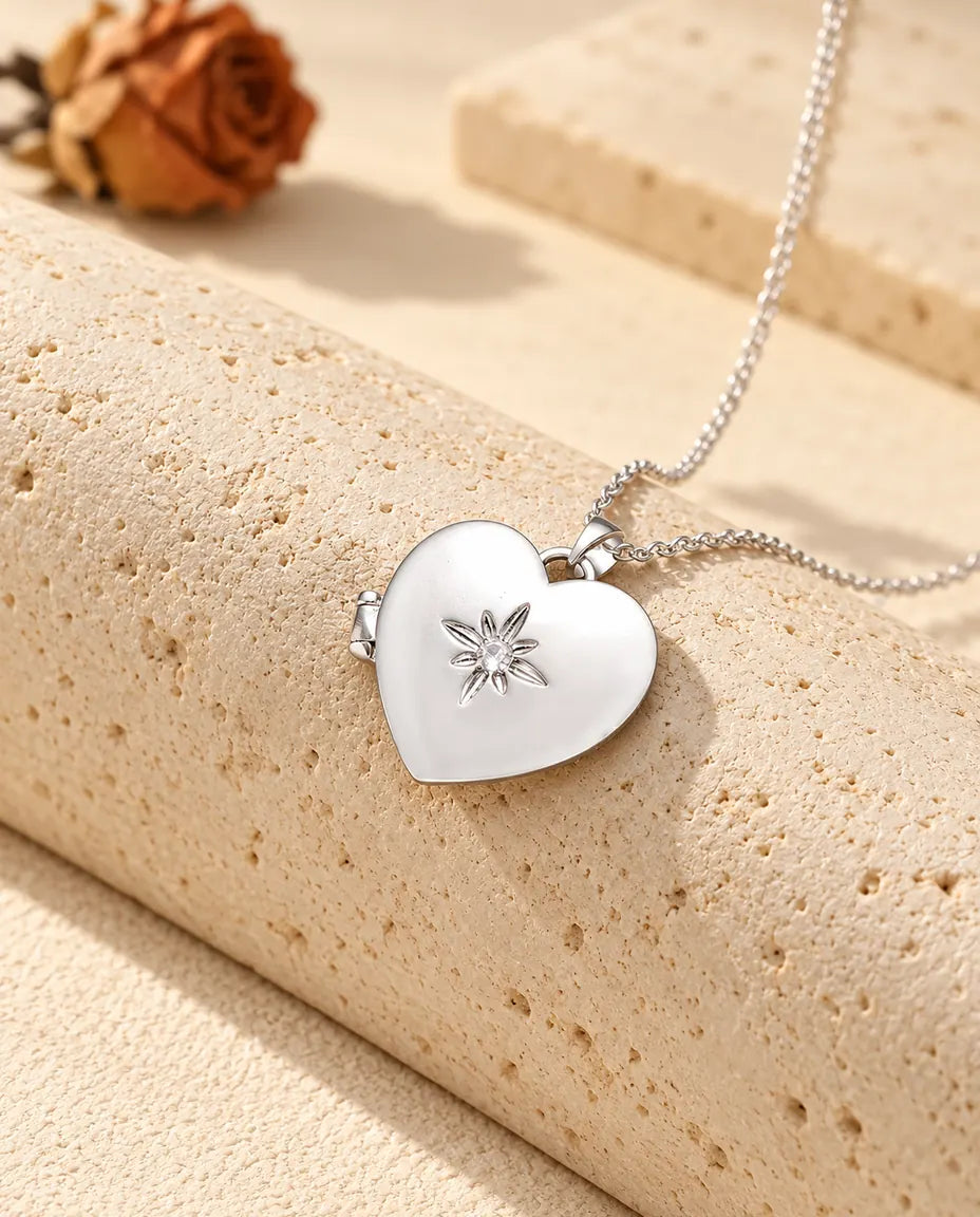 Personalized satin flower heart photo locket necklace in silver tone with a small starburst flower, resting on a travertine block