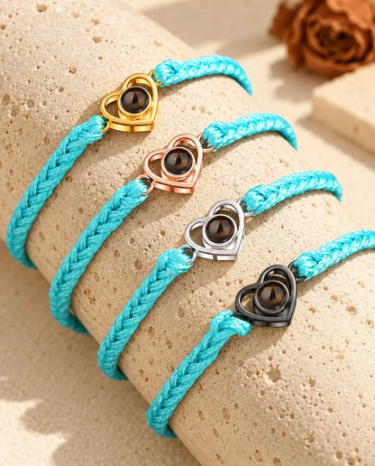 Four blue braided cord bracelets with gold tone, rose gold tone, silver and black open heart charms on a travertine block