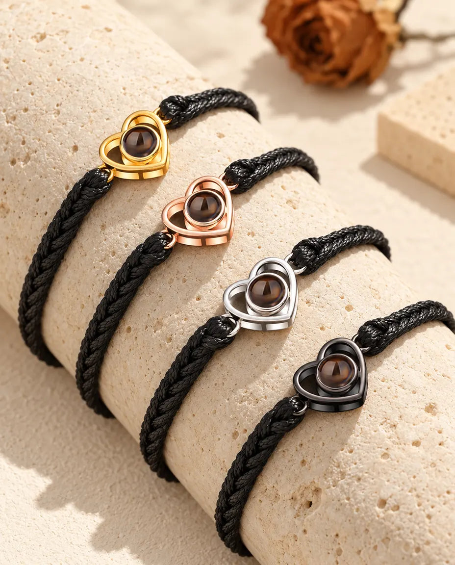 Four black braided cord bracelets with open heart charms in each color on a travertine block