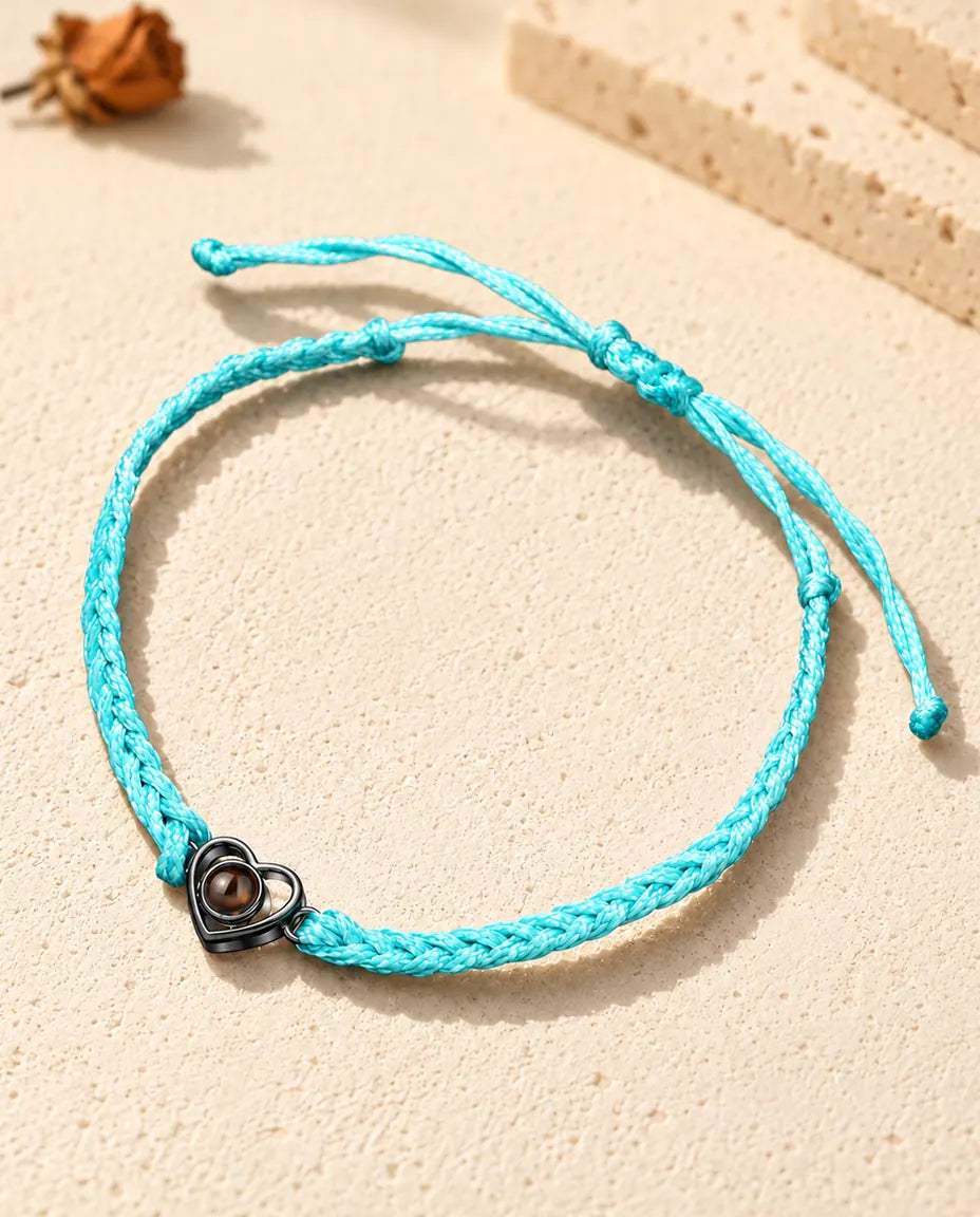 Black open heart charm on a blue braided cord holding a brown projection stone