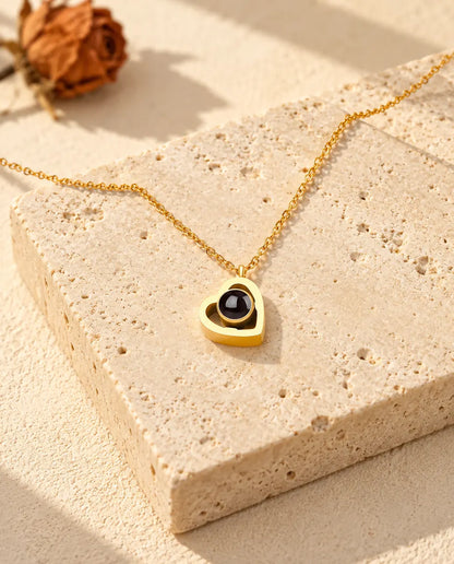 Gold tone double heart photo projection necklace lying on a travertine block