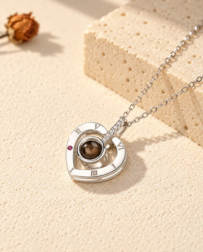 Personalized 925 sterling silver Roman numeral heart photo projection necklace on cream plaster beside travertine