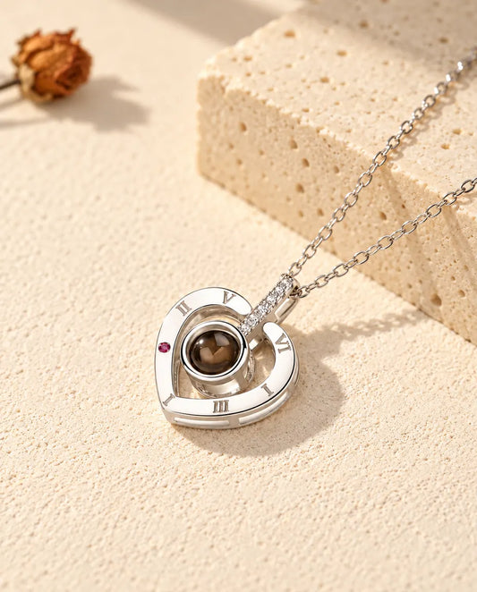 Personalized 925 sterling silver Roman numeral heart photo projection necklace on cream plaster beside travertine