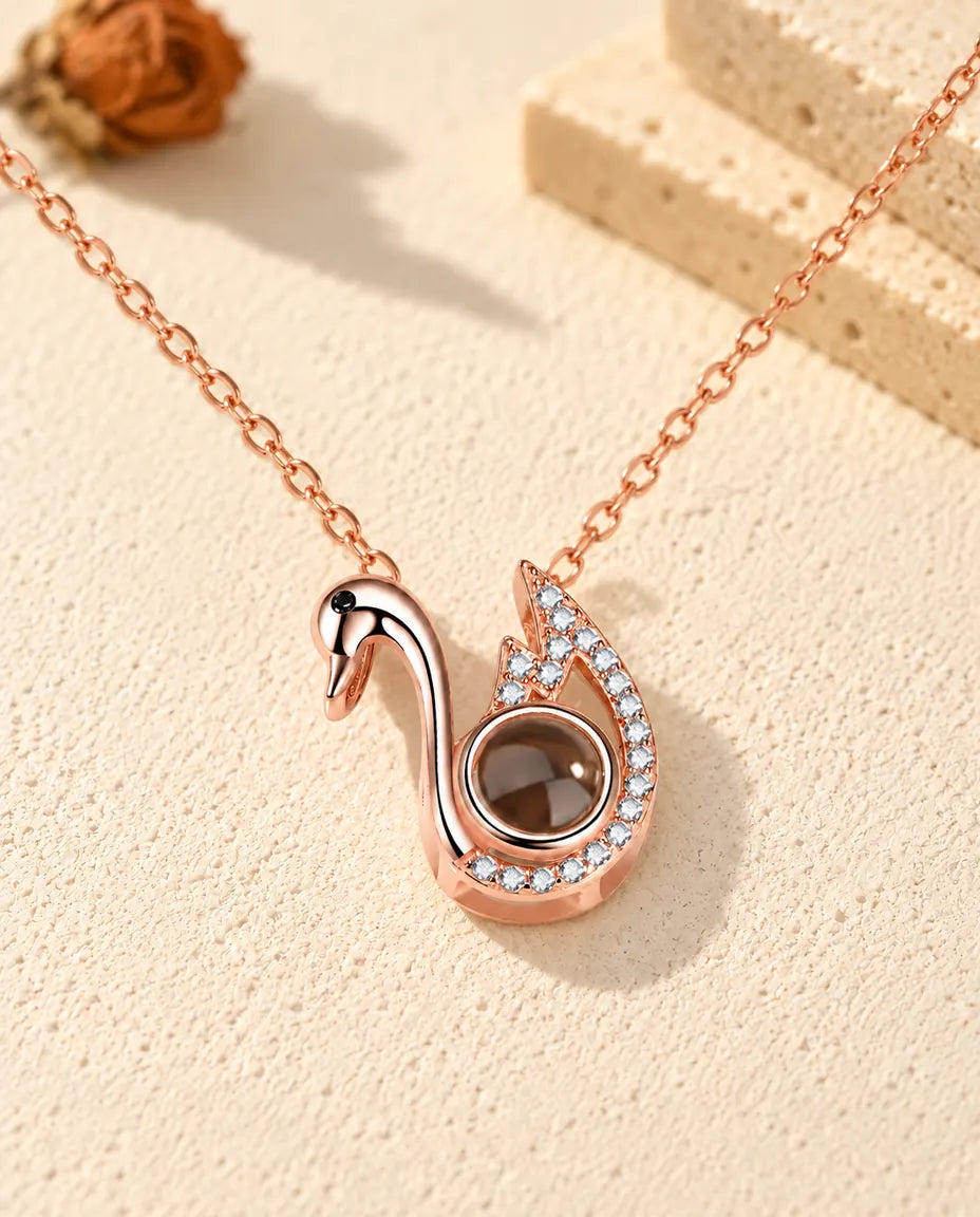 Personalized rose gold tone swan photo projection necklace on cream plaster beside travertine