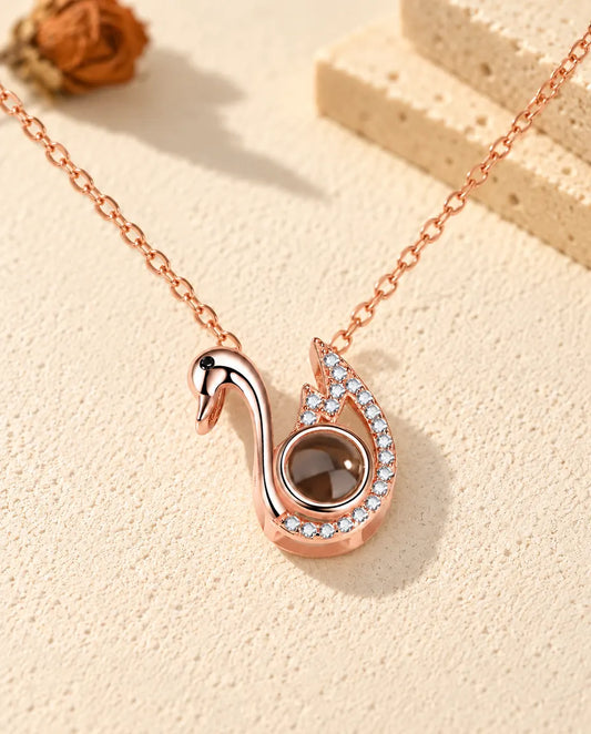 Personalized rose gold tone swan photo projection necklace on cream plaster beside travertine