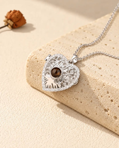 Personalized tree of life heart locket necklace in silver tone with a brown projection stone, resting on a travertine block