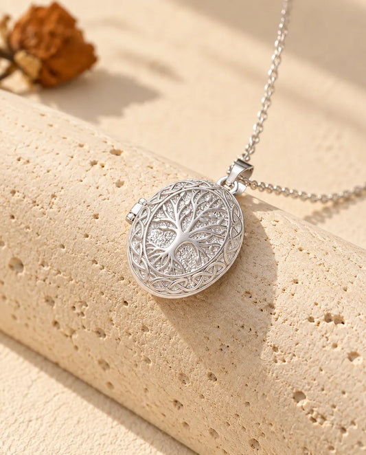Personalized oval tree of life photo locket necklace in silver tone with a Celtic knot border, draped over a travertine block