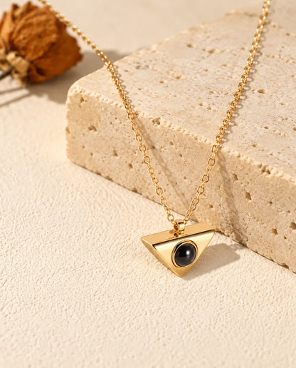 Gold tone triangle projection necklace hanging over a travertine block