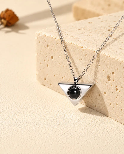 Silver tone triangle projection pendant seen at an angle on travertine
