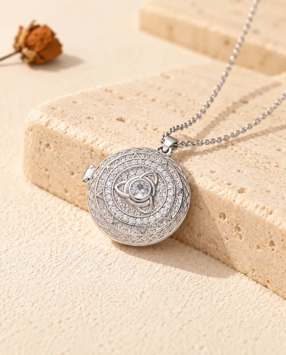 Personalized round trinity knot photo locket necklace in silver tone with cubic zirconia, resting on a travertine block