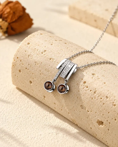 Personalized two photo projection necklace in silver tone with a pave slide and two brown projection stones on a travertine block