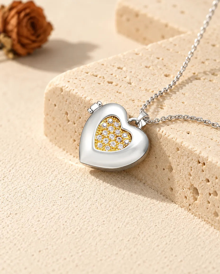 Personalized two-tone pave heart photo locket necklace in silver tone with a gold tone pave inner heart, resting on a travertine block