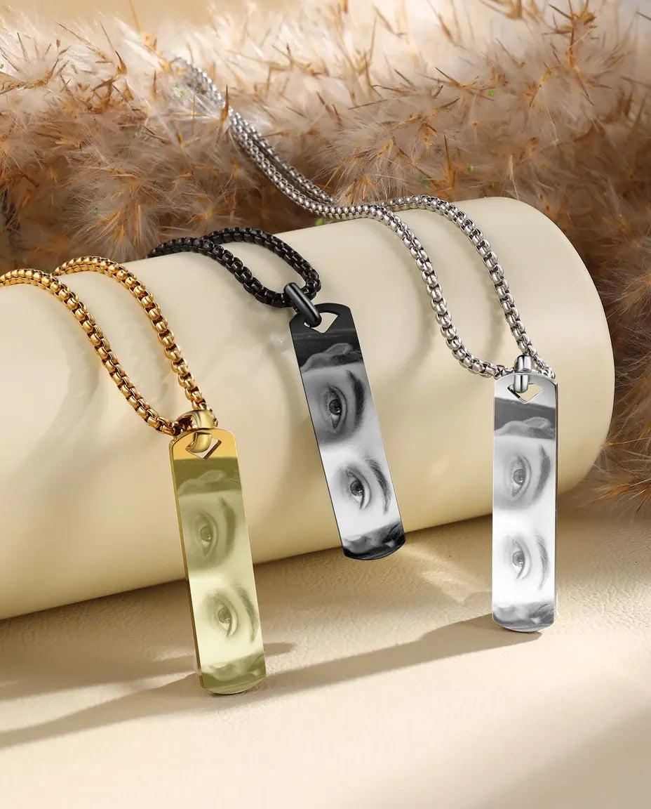 Three photo bar necklaces in gold, black and silver on a cream surface