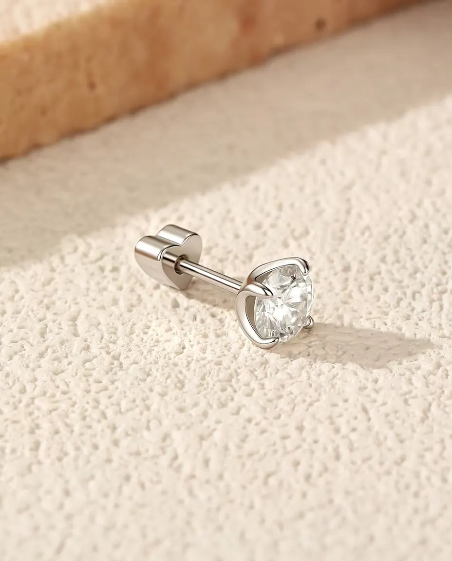 Round Moissanite Four-Prong Stud Earrings in 925 Sterling Silver - lying on its side on a cream textured surface, heart-shaped back on the post