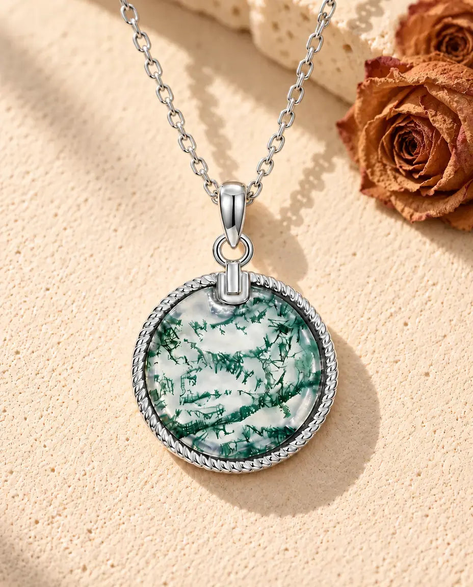 Round Moss Agate Medallion Necklace in 925 Sterling Silver - lying on a cream textured surface beside a travertine block