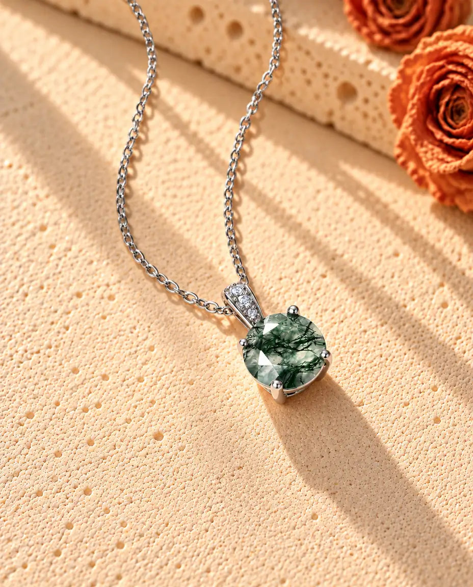 Round Moss Agate Solitaire Necklace in 925 Sterling Silver - seen at an angle on a cream textured surface