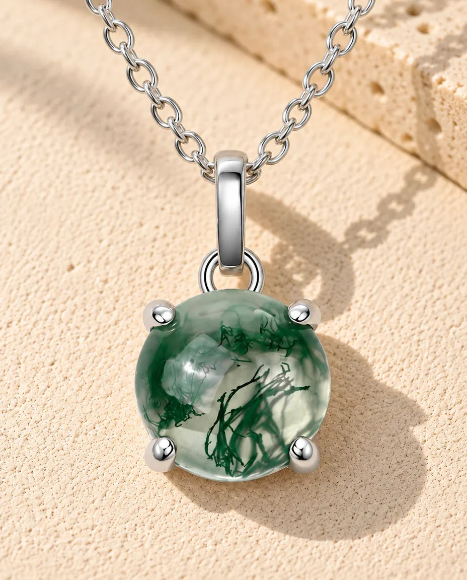 Round Moss Agate Solitaire Necklace in 925 Sterling Silver - lying on a cream textured surface beside a travertine block