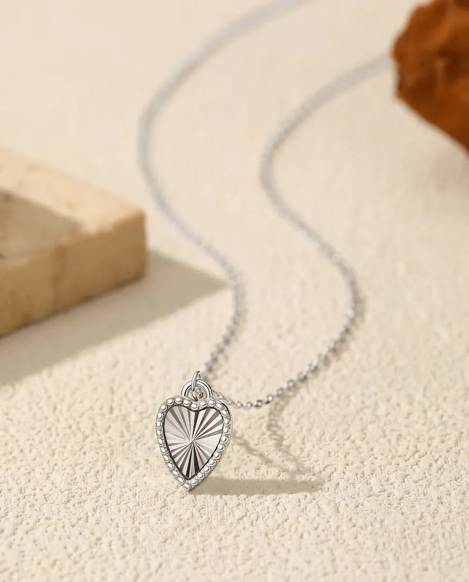 Heart Pendant Necklace in 925 Sterling Silver - pendant resting on a cream surface beside a travertine slab