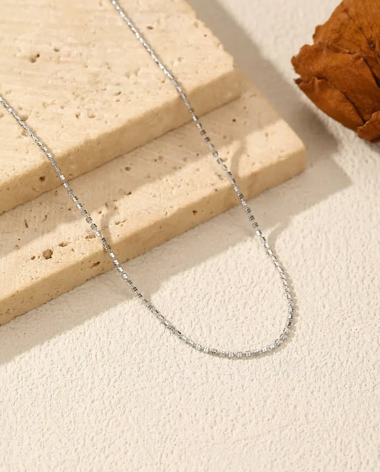 Sparkle Chain Necklace in 925 Sterling Silver - draped across a cream surface beside a travertine slab