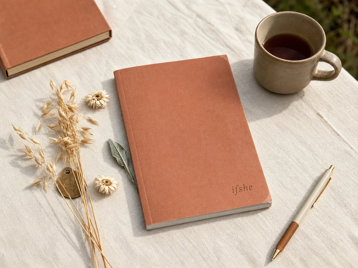 Terracotta cloth-cover pet wedding planning workbook on cream linen with dried wildflowers, brass pet ID tag, ceramic mug of tea, natural outdoor morning light